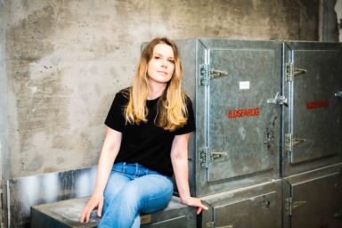 Trude Lorentzen, journalist og podkastskaper, sitter ved et metallskap merket "ildfarlig".