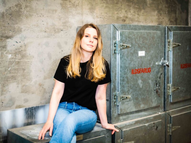 Trude Lorentzen, journalist og podkastskaper, sitter ved et metallskap merket "ildfarlig".